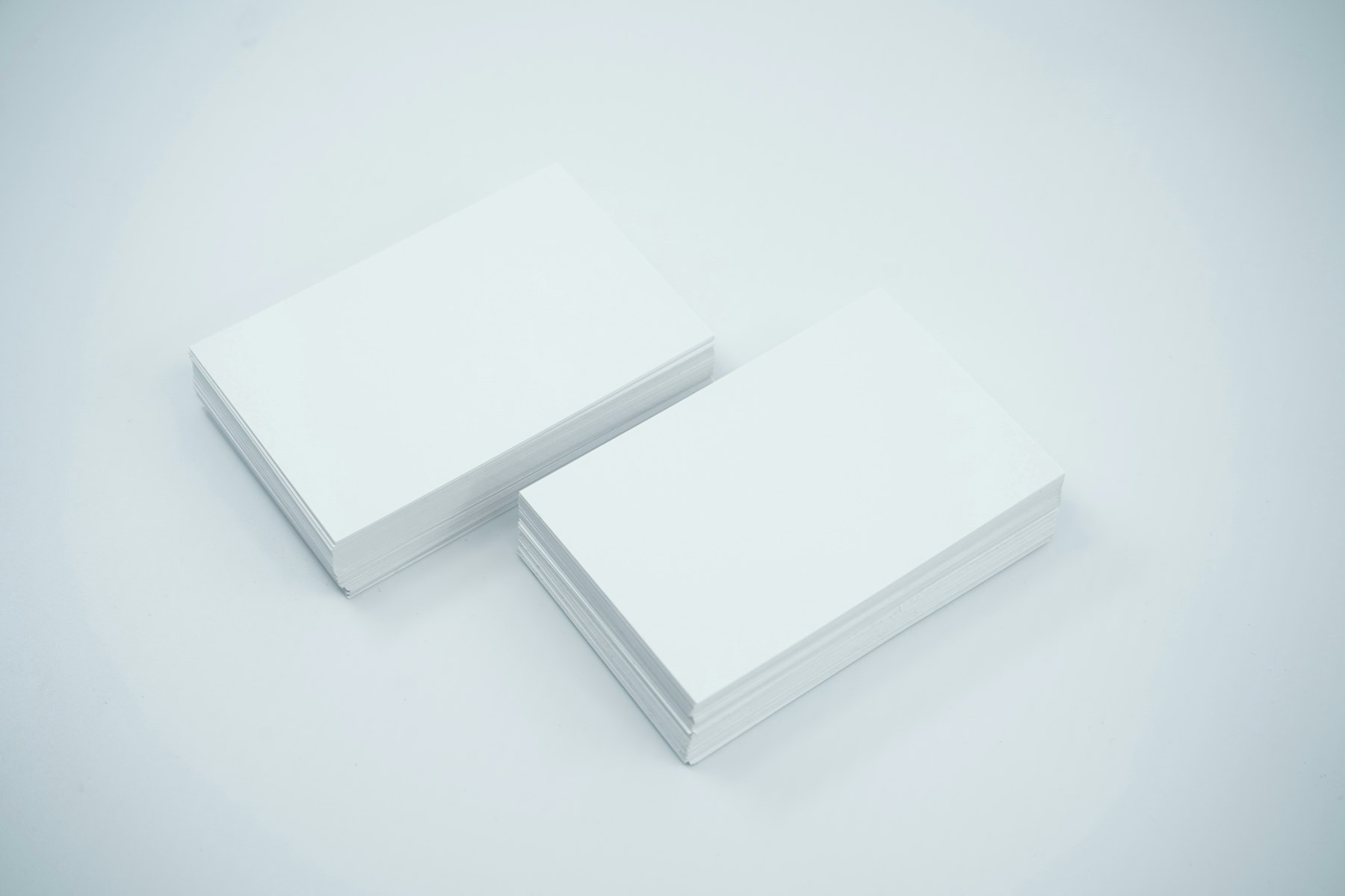 Two stacks of white business cards on a pale grey surface
