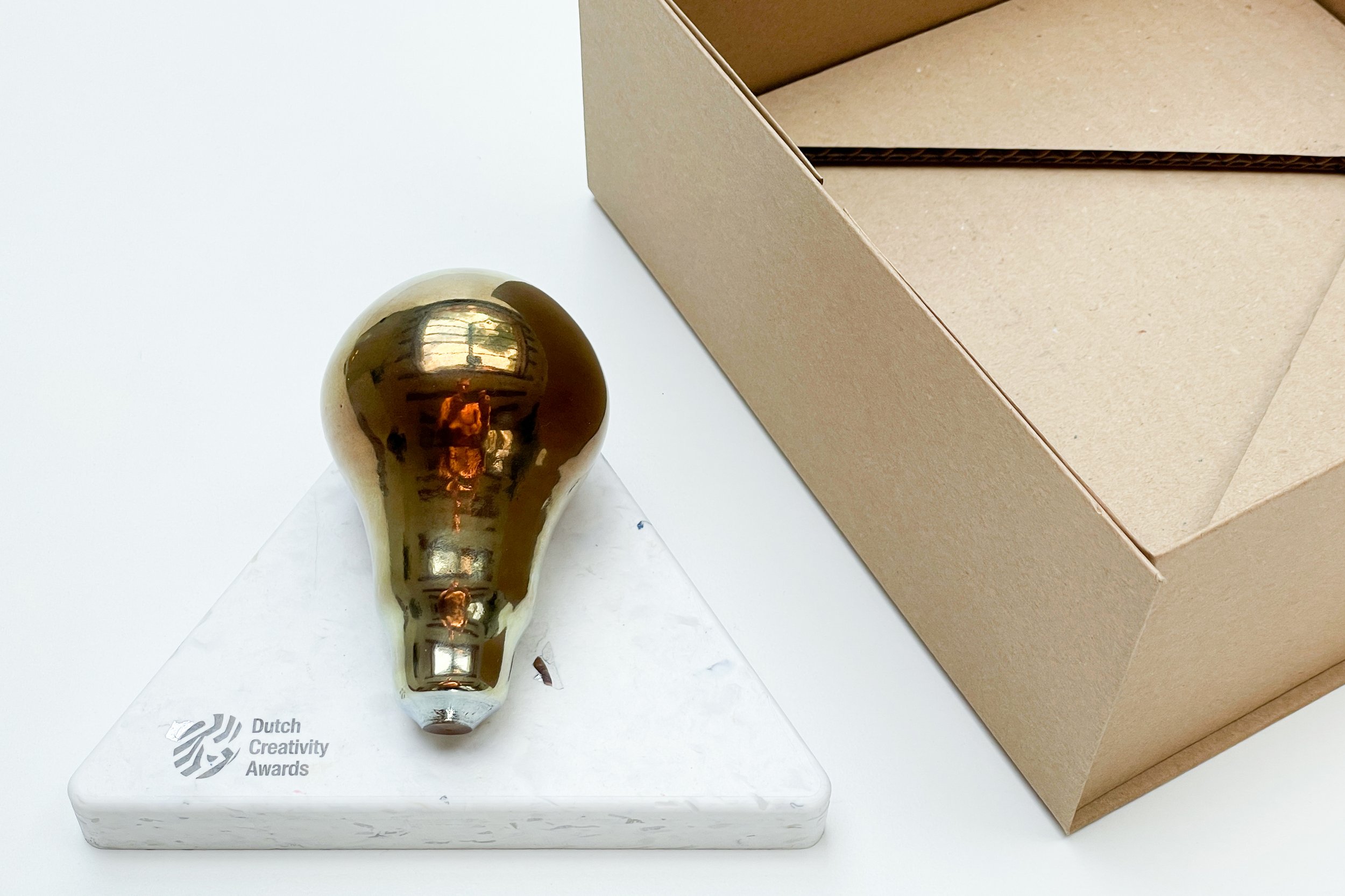 Image of a golden glass award on a recycled plastic award base and a untreated cardboard box with cardboard inlay