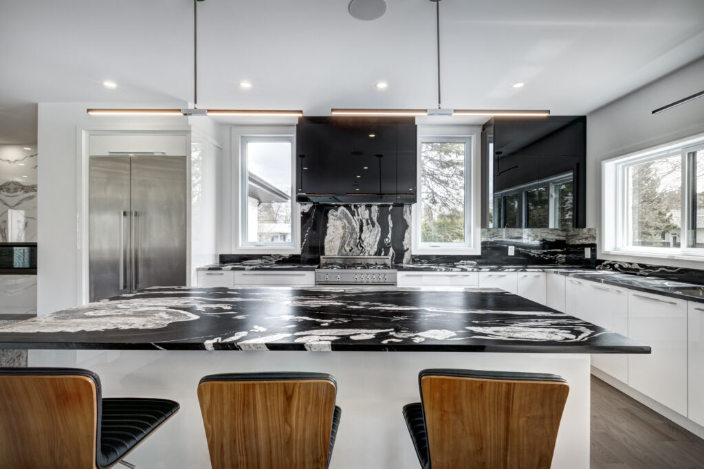 Luxury kitchen renovation with bold black and white marble island and backsplash, sleek black cabinetry, stainless steel appliances, and wraparound windows, showcasing B&Y Reno Corp’s high-contrast modern design