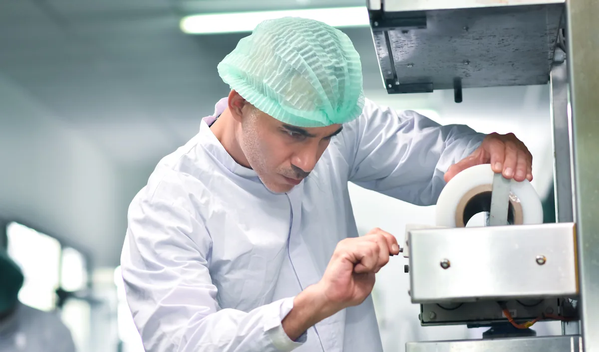 Technician in a hairnet adjusting part of a packing machine