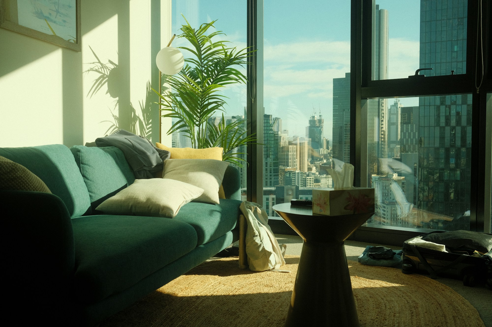 Apartment living room with a green velvet sofa and full-height windows over the city