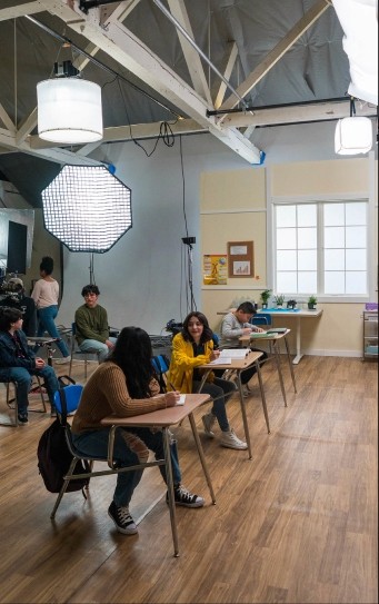 Child actors portraying students sit on a School Set built on the main floor of Particle Studio.