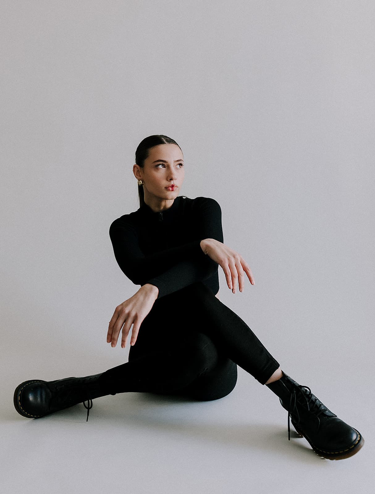 The model gazes off to the side while sitting casually on the floor at Revelator Studio in Shreveport, photographed by Justin Posey, highlighting the clean and modern aesthetic of the studio.