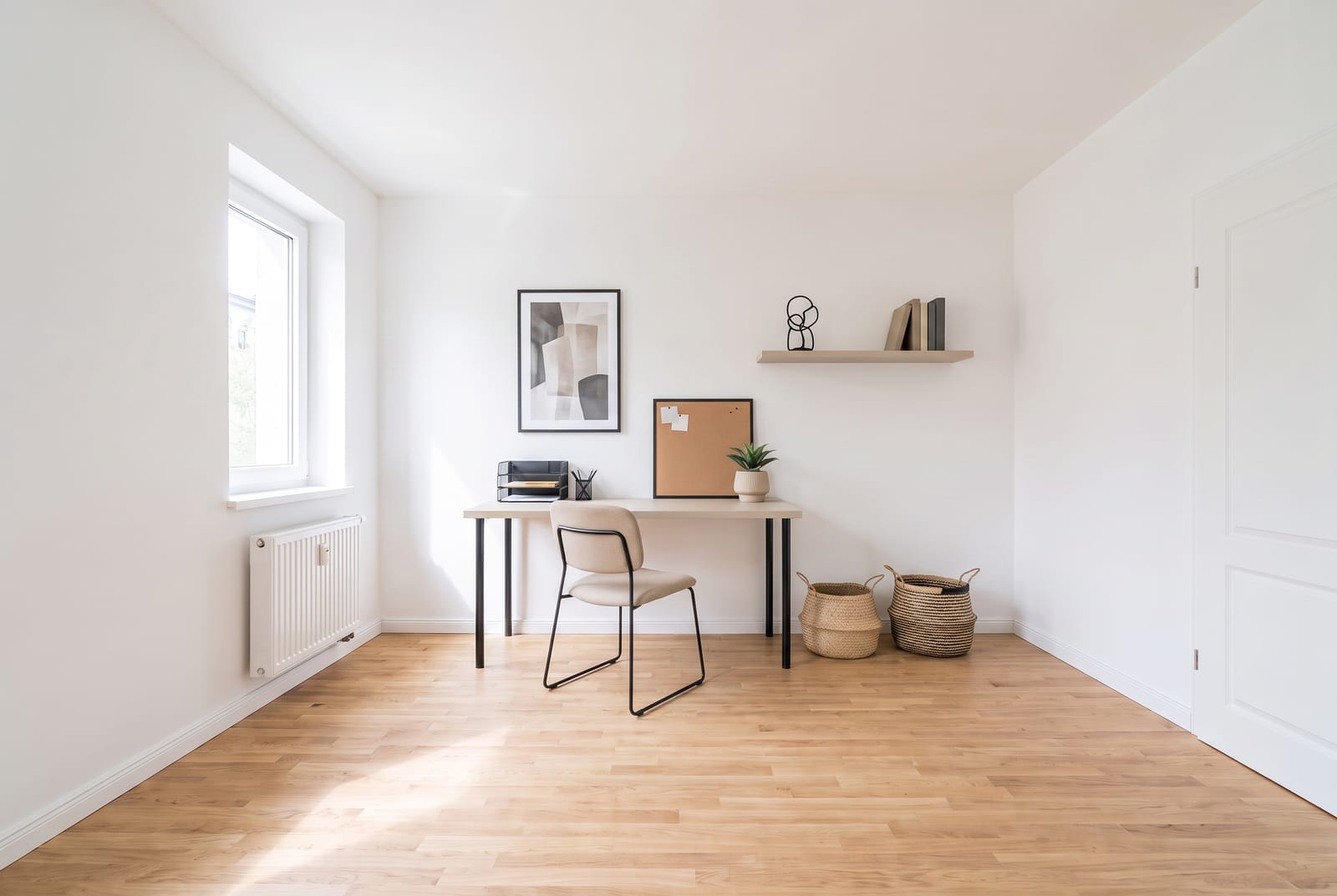Schlichter Arbeitsplatz mit schmalem Schreibtisch, einfachem Stuhl, Wandbord mit wenigen Dingen und zwei Körben am Boden