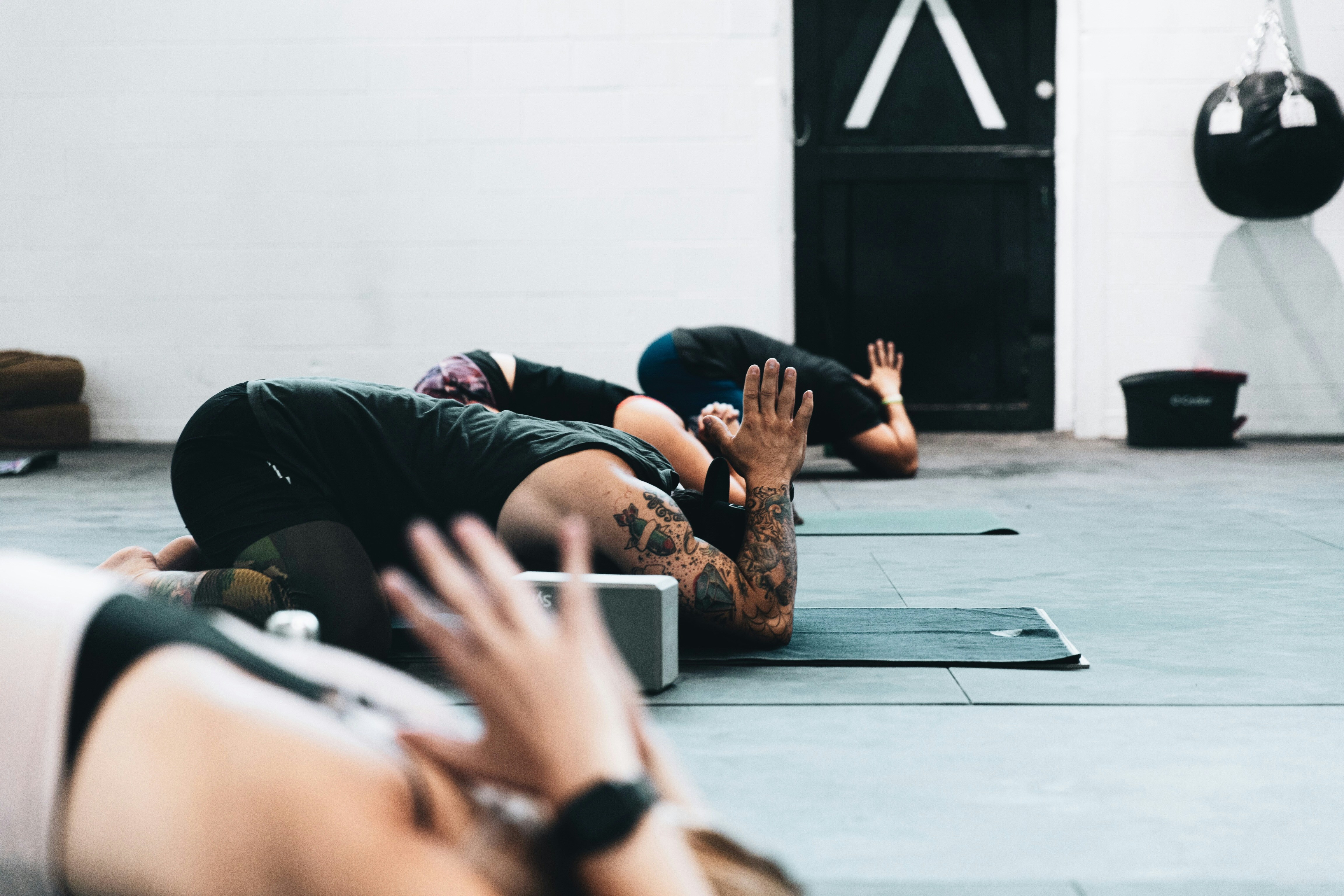 A group of people in childs pose position doing yoga on matts in a gym.