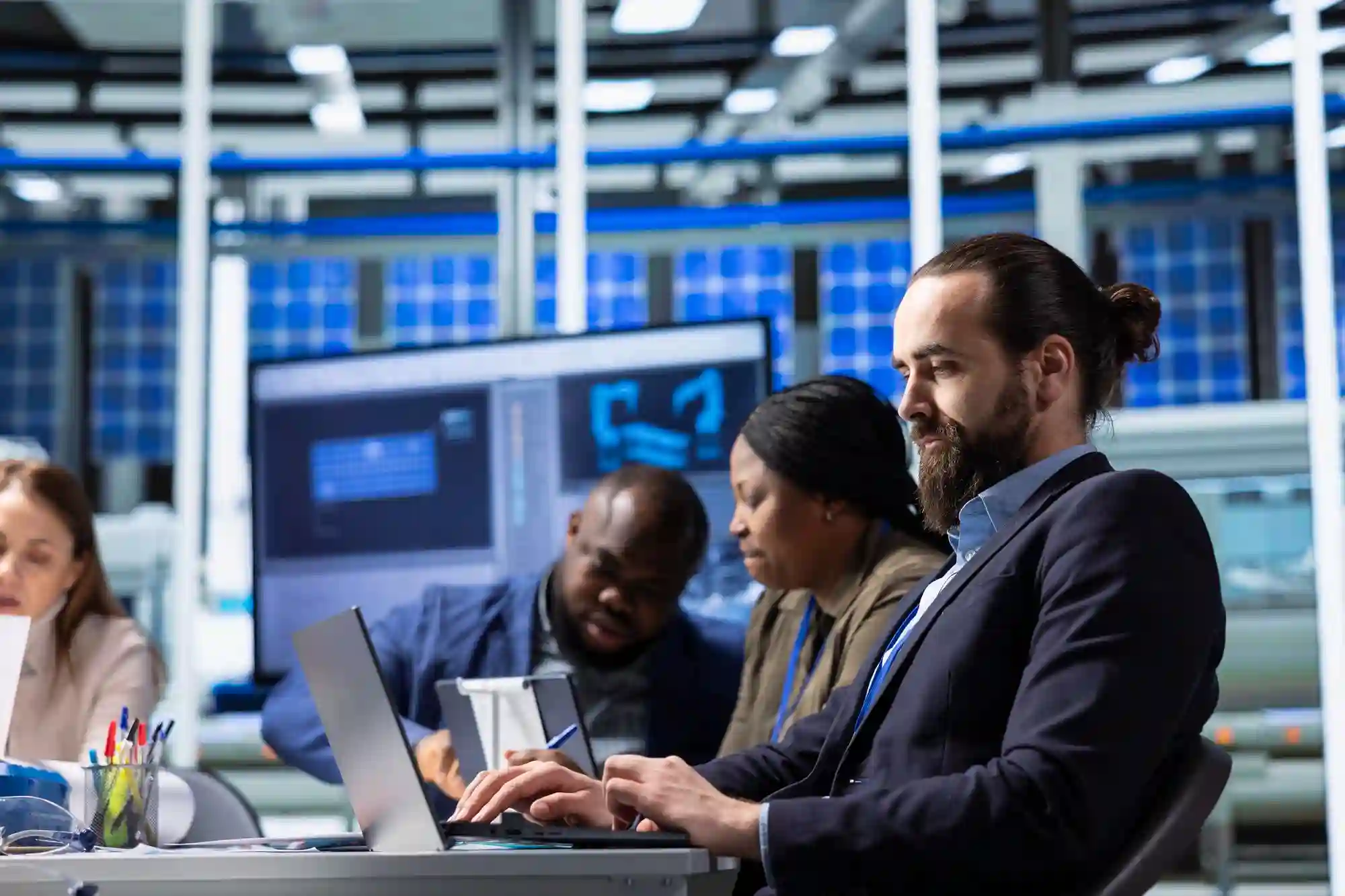 A focused professional team working on laptops and analyzing data on large screens in a high-tech corporate environment.