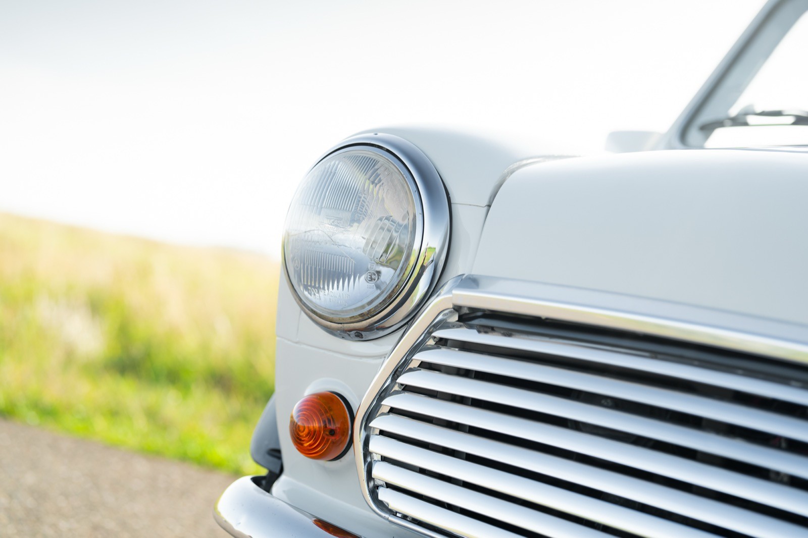 Close-up of the front of a classic car, featuring a round headlight and a striped grille, set against a green background.