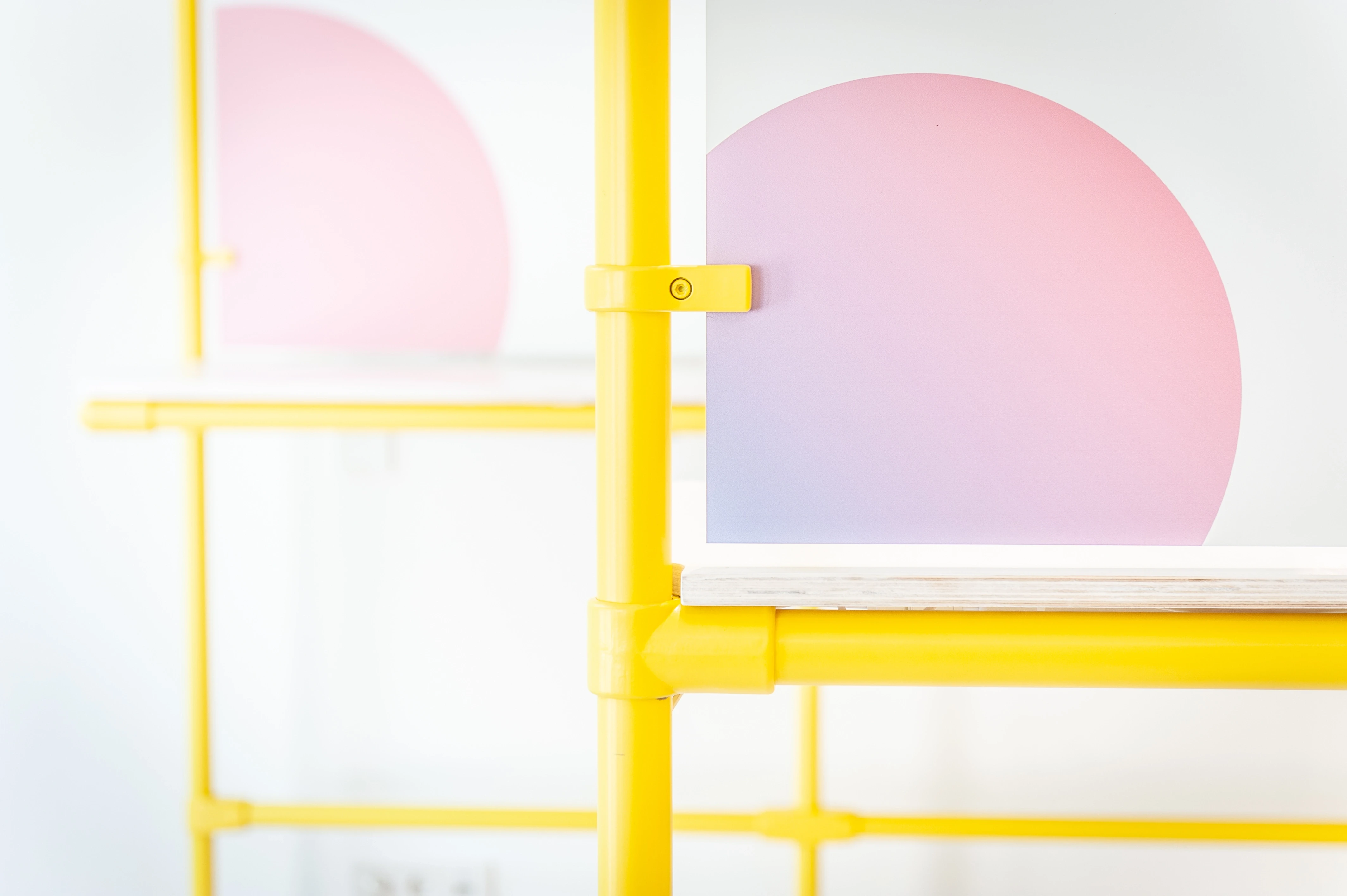 Close-up of a yellow tubular scaffold shelf at EHEALTH-TEC with acrylic panels showing a pink-to-purple circular gradient print on a white background.