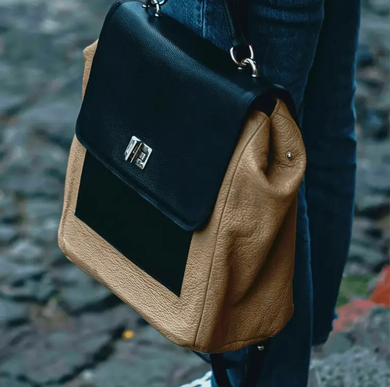 Tan and black leather FeLuxe bag carried over the shoulder on a cobbled street