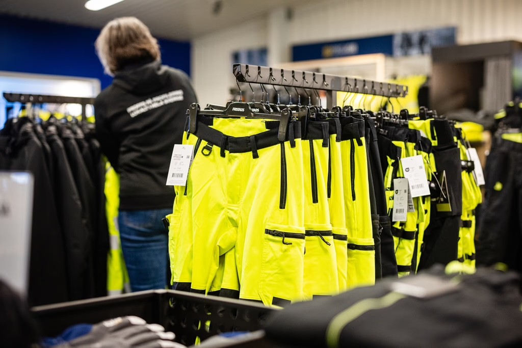 Kund granskar arbetskläder och varselkläder i 4Signs butik, exempel på profilkläder.