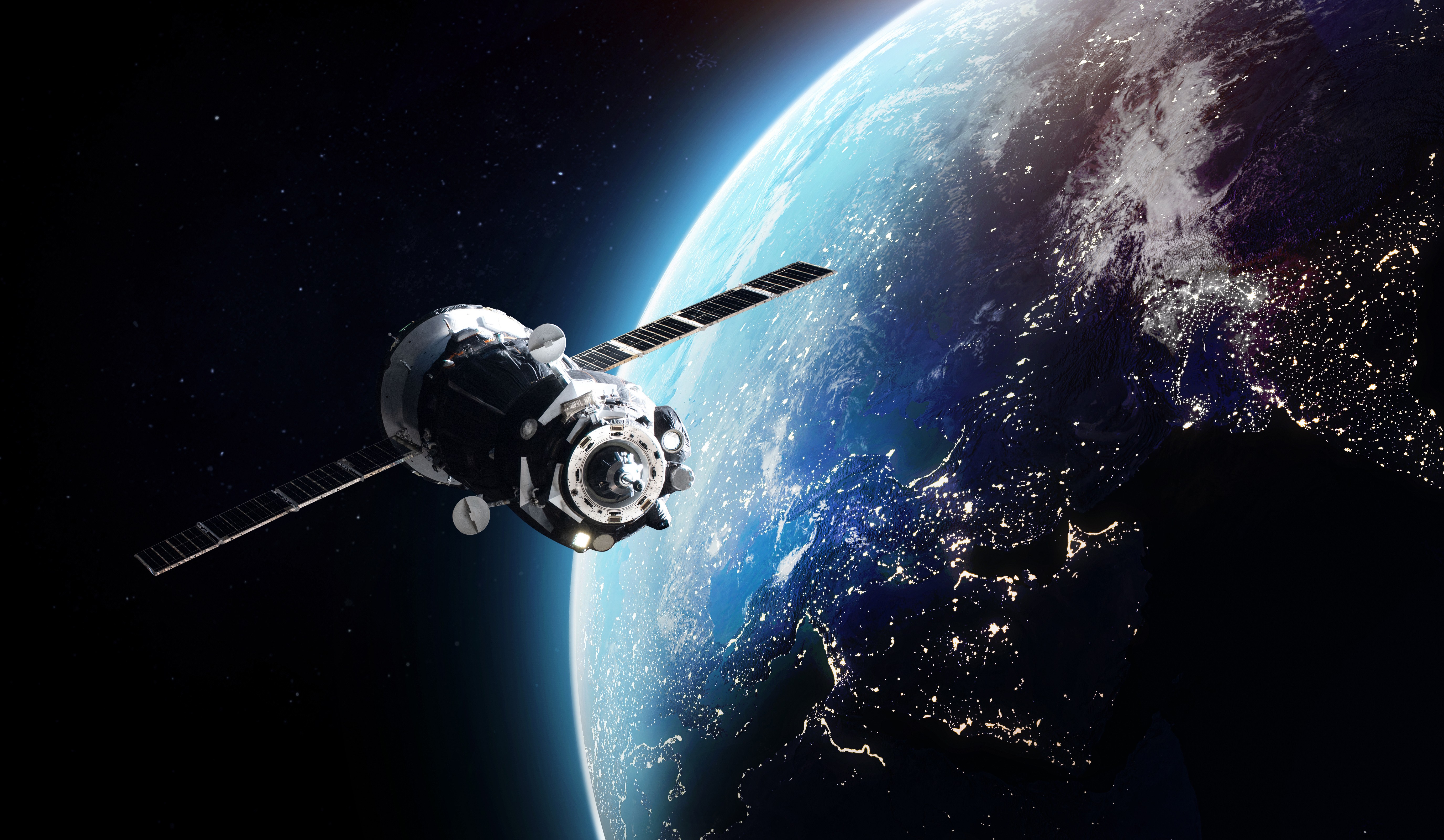 A satellite with solar panels orbits above Earth, showcasing a vibrant view of the illuminated city lights on the planet's surface and the deep blue curvature of the Earth against the backdrop of space.
