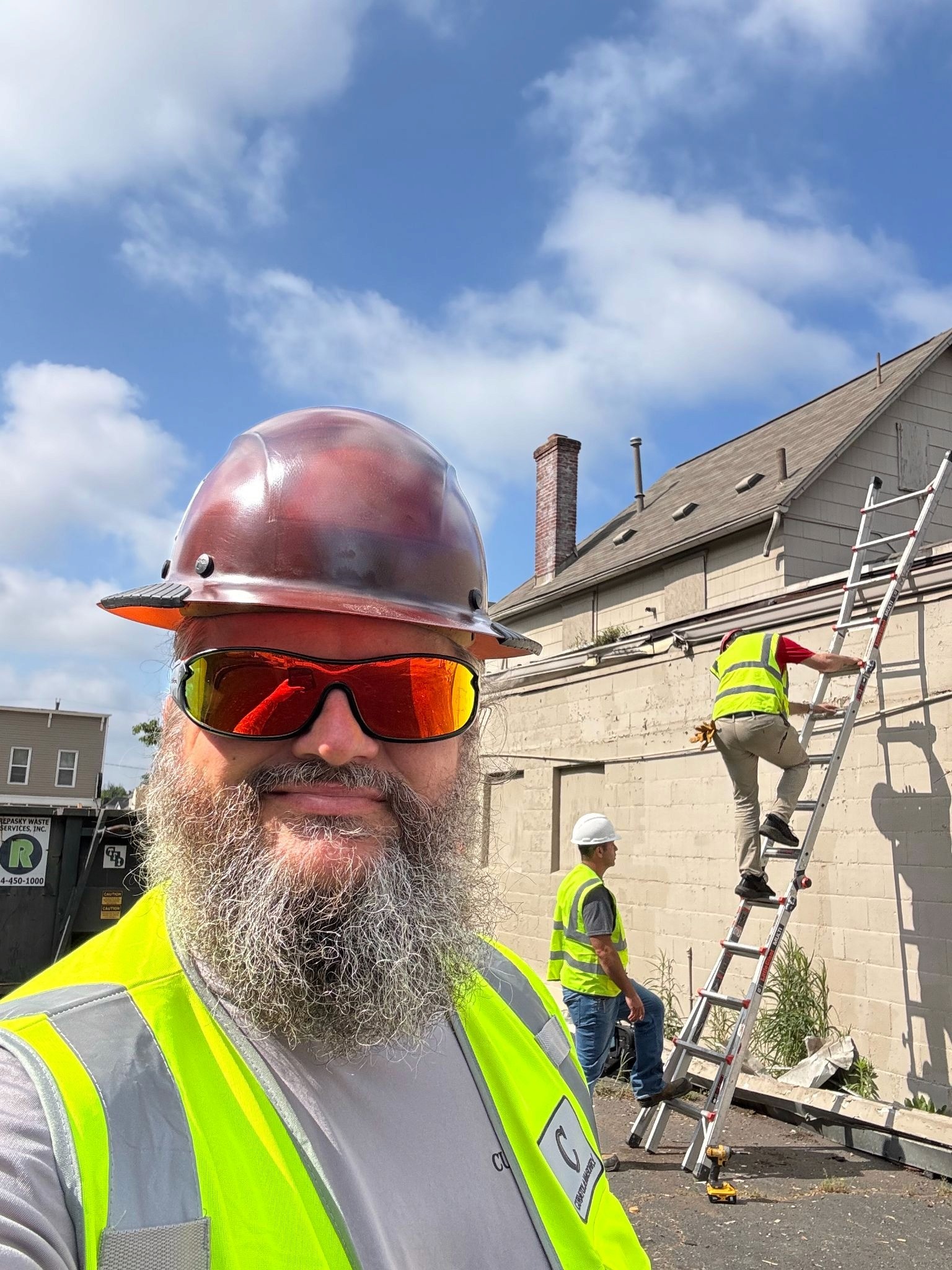 Construction worker in safety gear at building repair site with crew using a ladder.