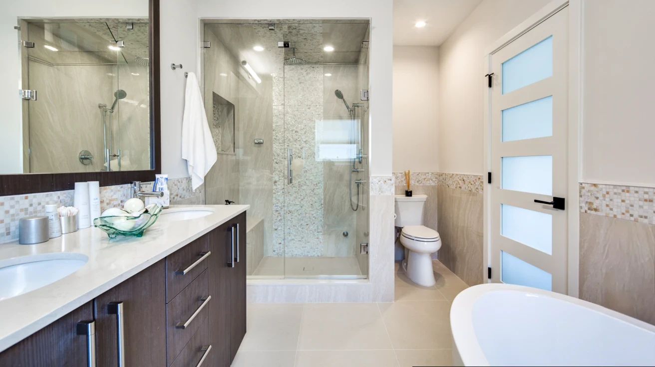 Spa-like luxury bathroom featuring frameless glass shower with pebble tile accent, freestanding soaking tub, dual vanities, and modern fixtures