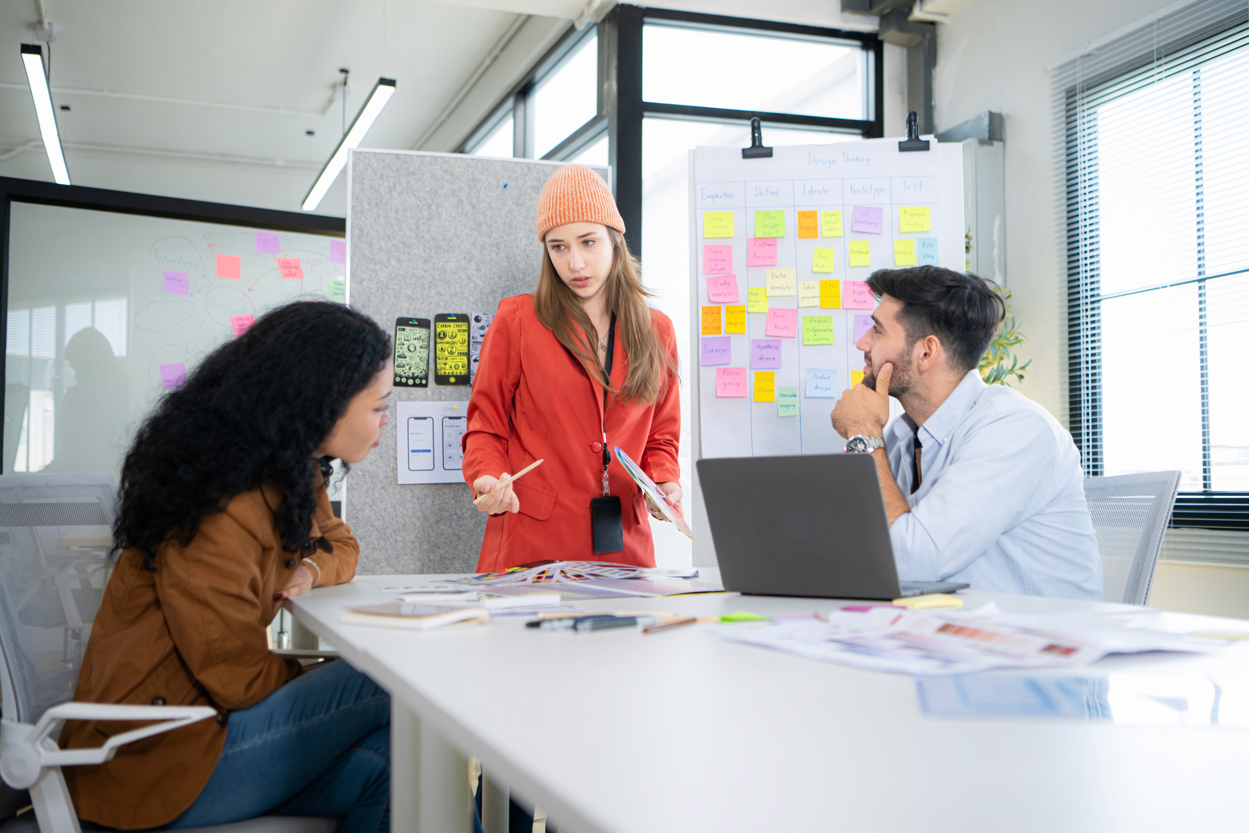 Three coworkers brainstorming at a desk in front of a wall of sticky notes.