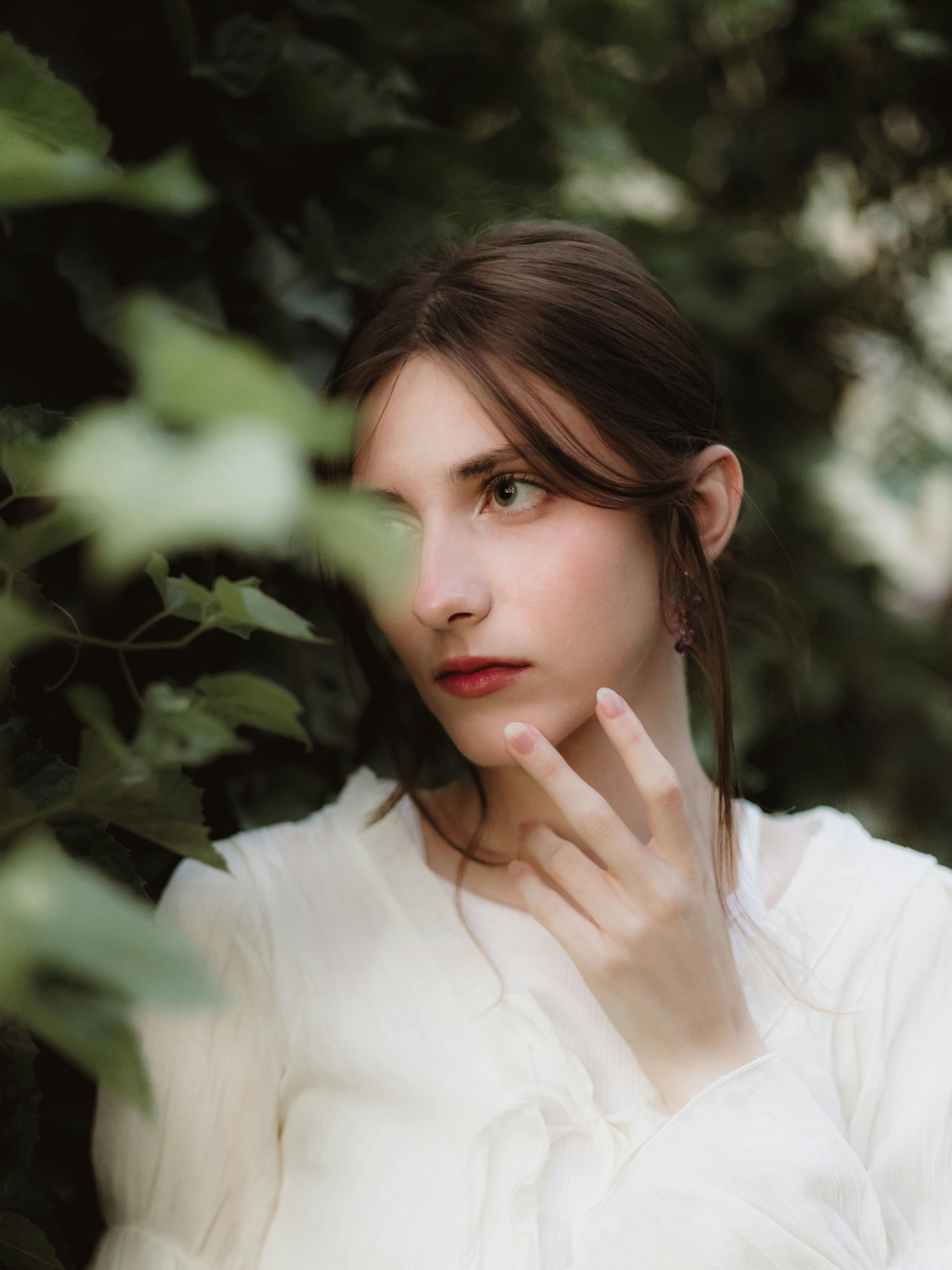 Young woman with hand near face in green foliage