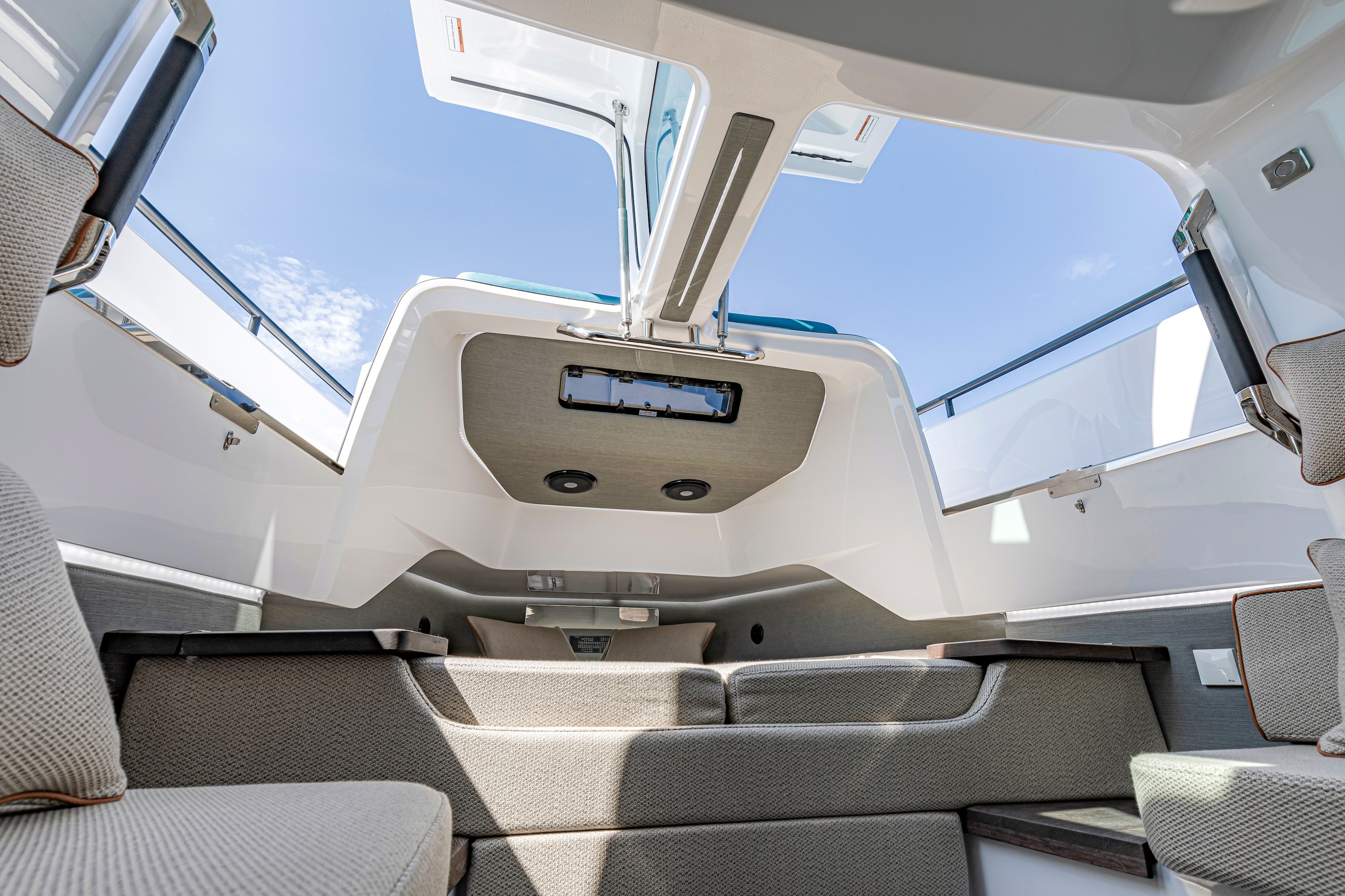 Modern yacht cabin interior with panoramic windows, retractable sunroof, and beige seating under clear blue skies.