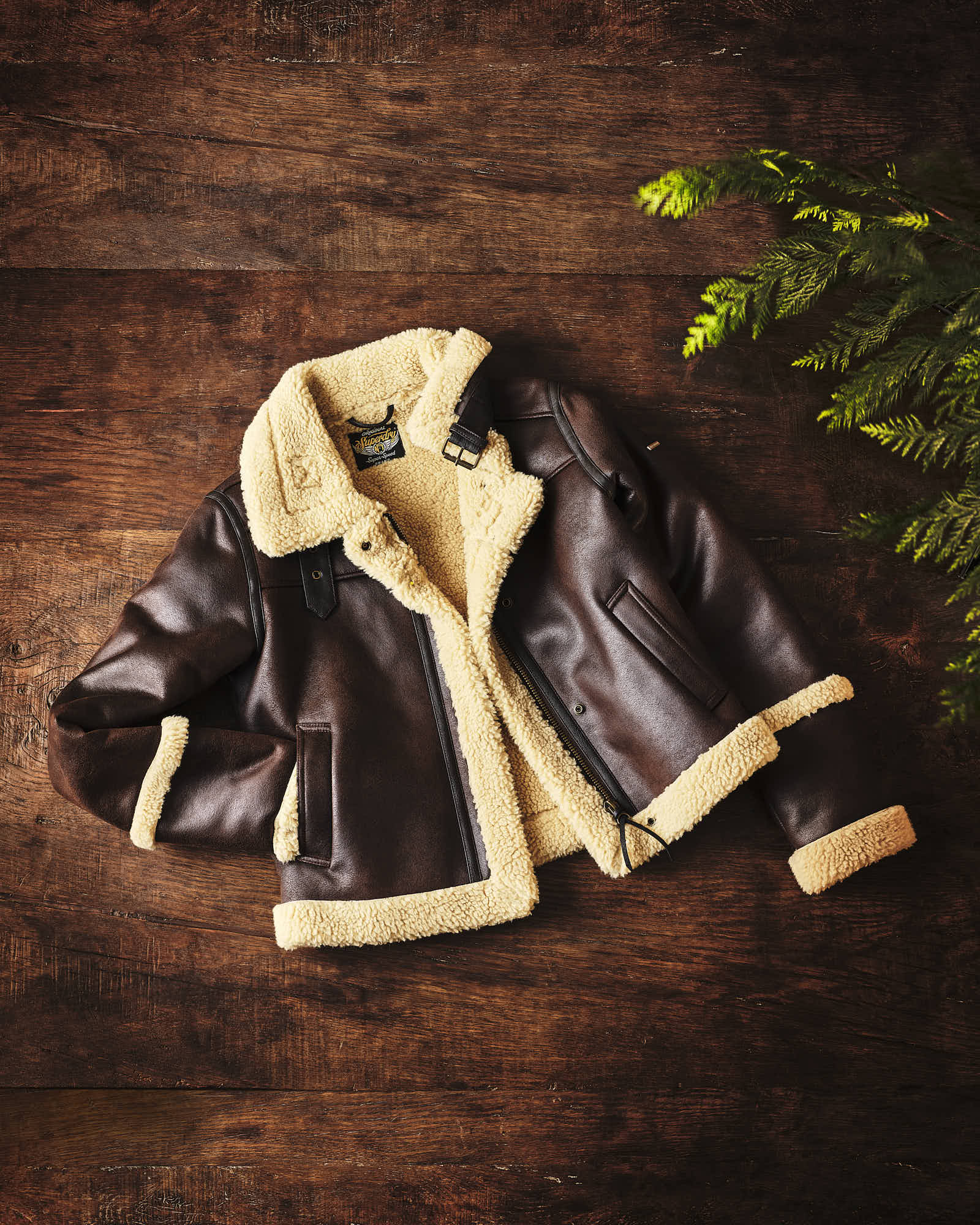 Brown shearling leather jacket on wooden background with green foliage