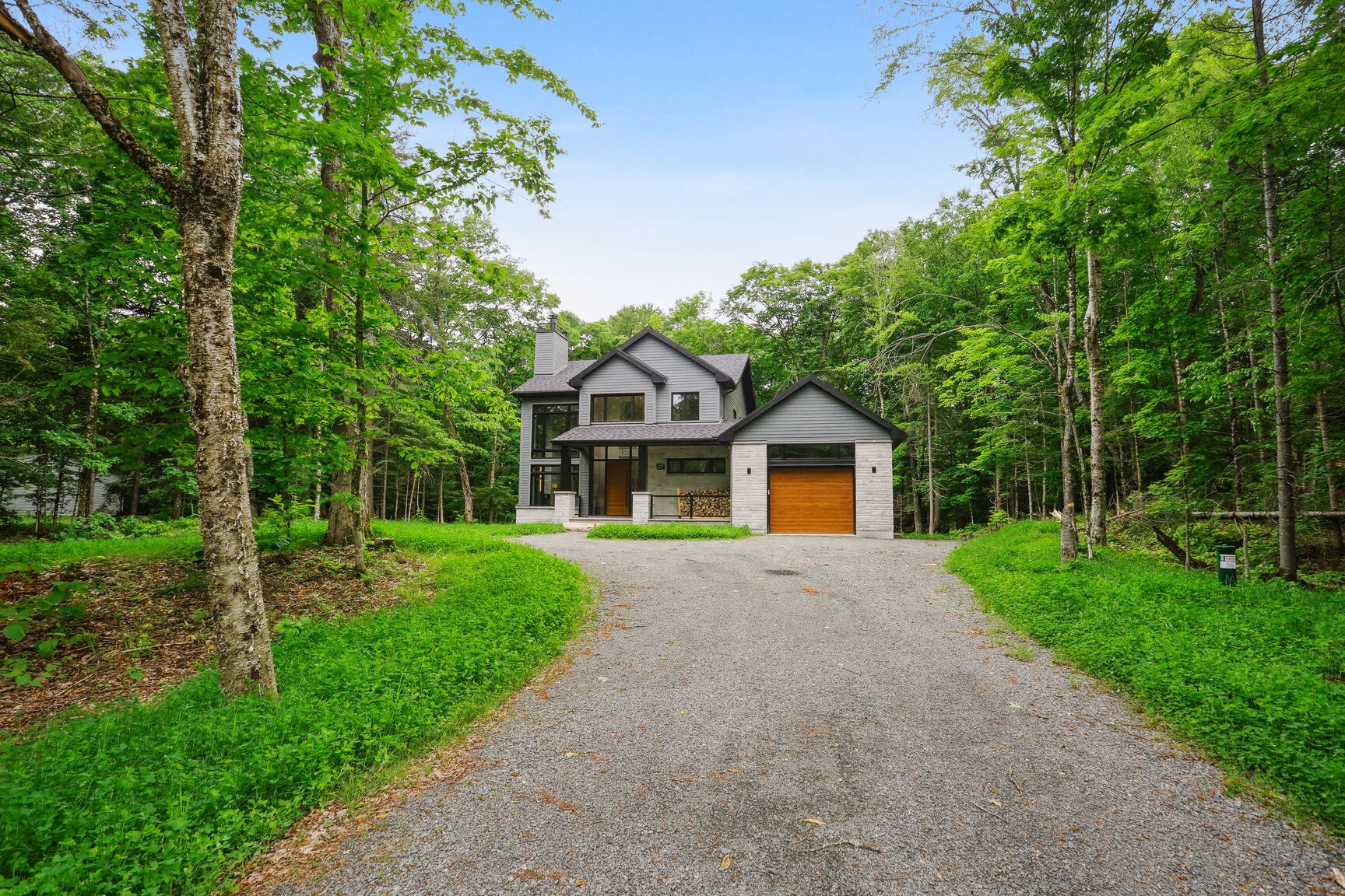 Façade avant et allée de gravier, maison contemporaine en milieu boisé.