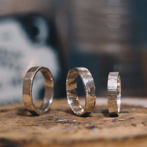 三个不同纹理的银戒指竖直排列在木质表面上，背景模糊。
