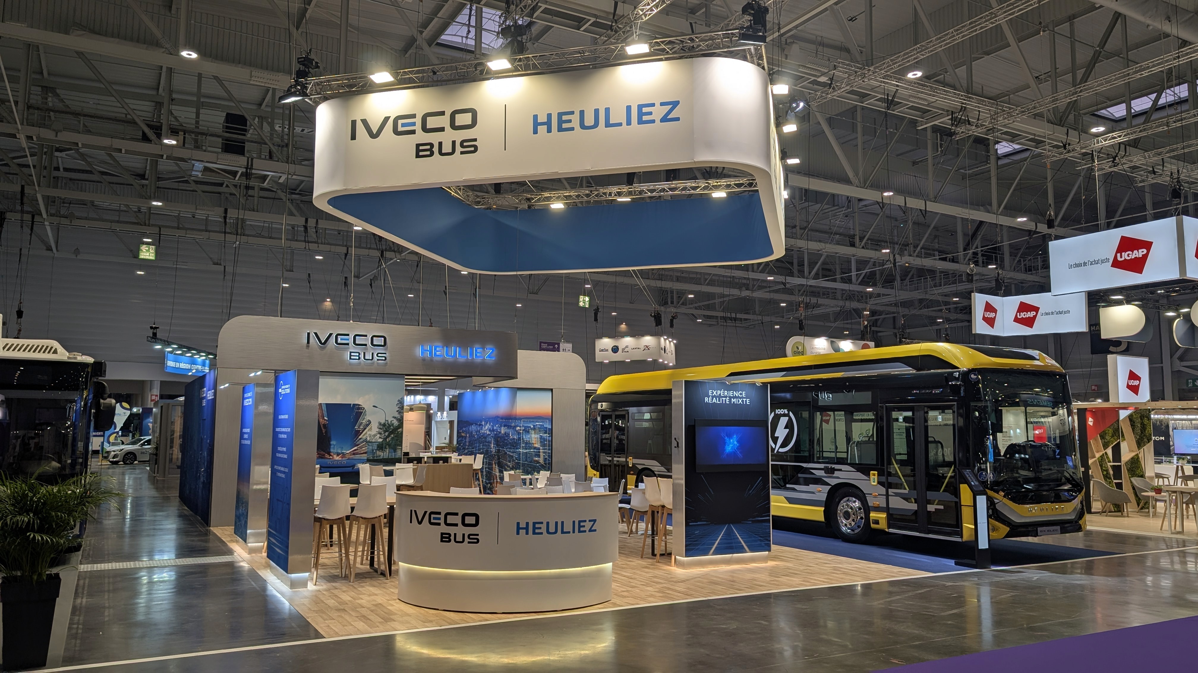 Stand IVECO Bus et Heuliez RNTP 2025 réalisé par Expace – vue frontale du stand commun avec bus exposé, signalétique bleue et jaune et espace visiteurs