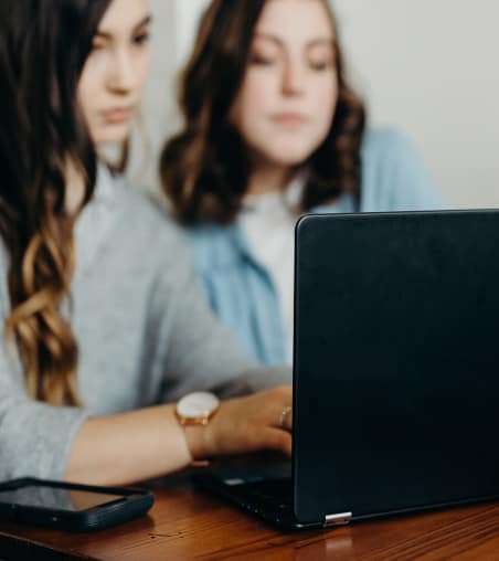 Two women working on a laptop sitting at the desk.