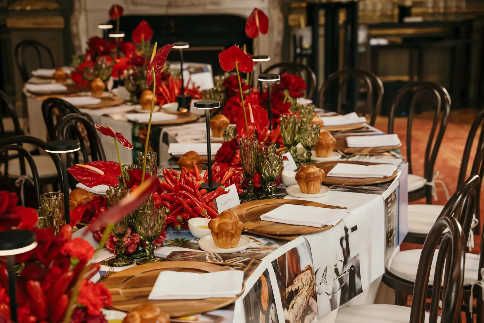 Mesa de banquete con centros de flores rojas, chiles frescos, lámparas de diseño y cristalería verde tallada.