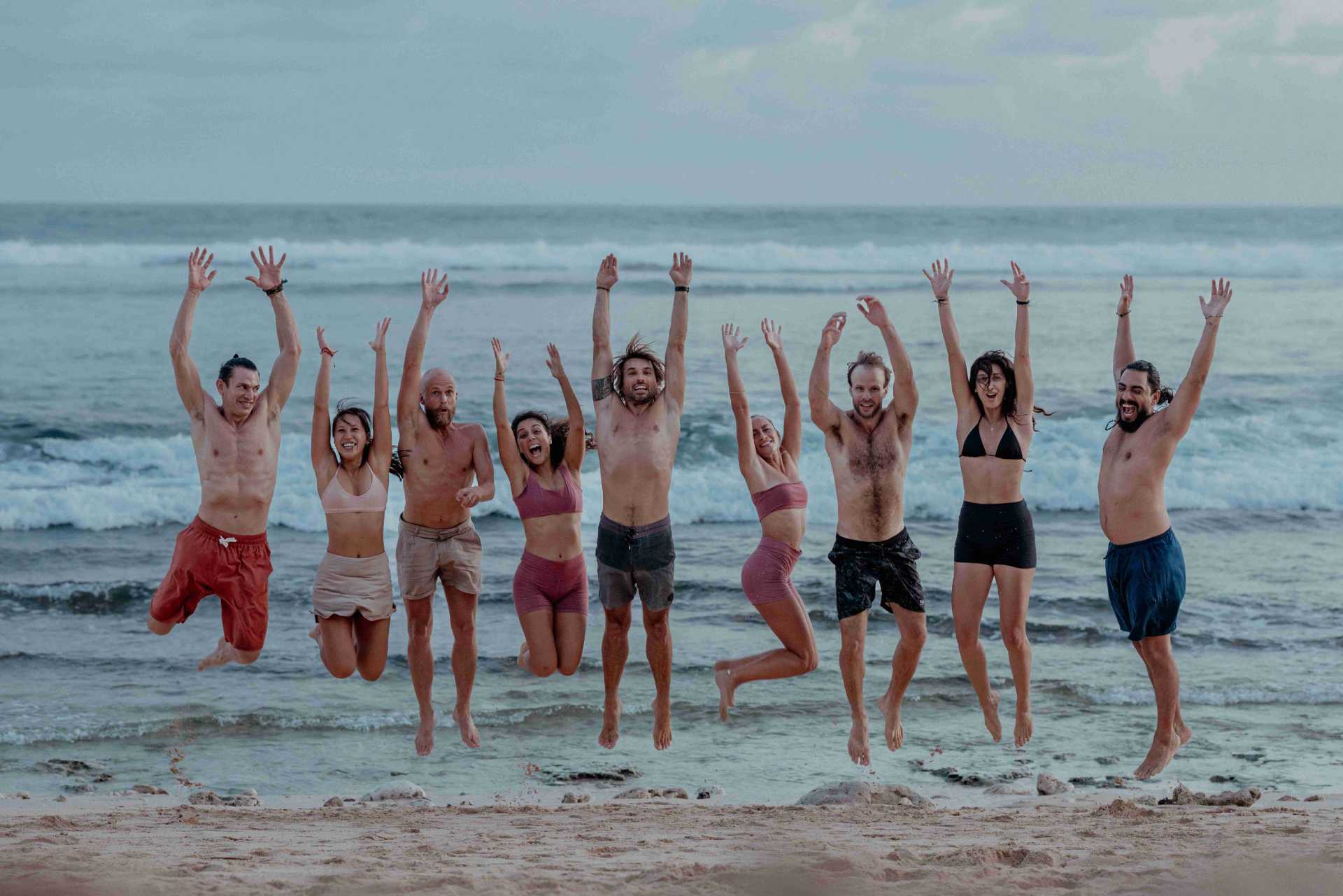 Happy yoga teacher training students jumping on the beach in Bali celebrating their graduation.