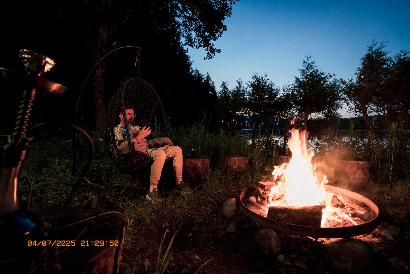 Homme assis près d’un feu de camp au crépuscule.