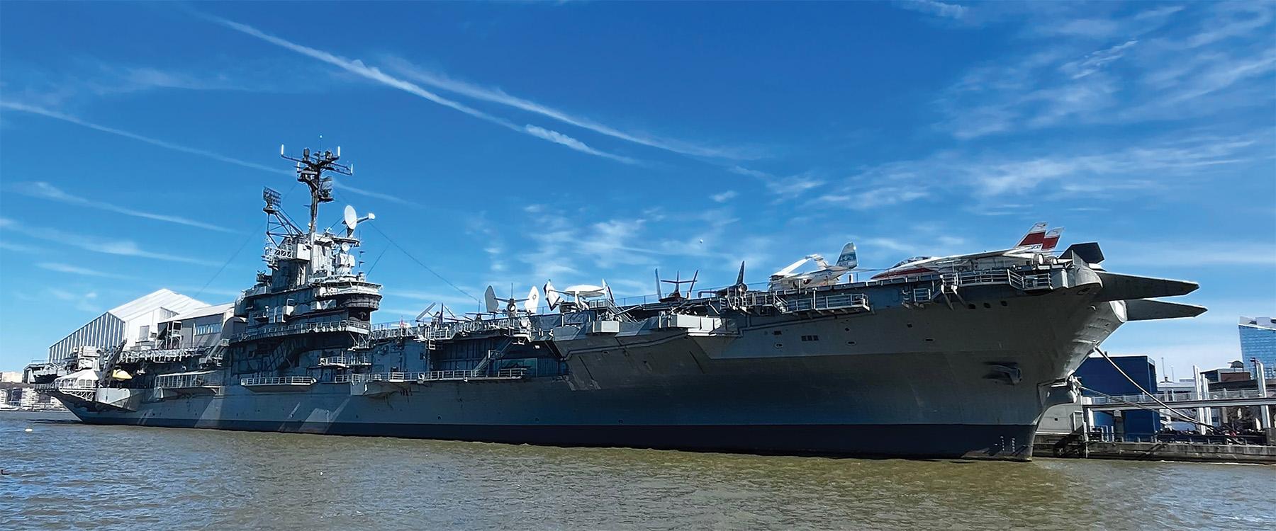 USS Intrepid aircraft carrier at the Intrepid Museum in New York City, seen docked on the Hudson River with military aircraft on the flight deck and the Manhattan skyline in the background