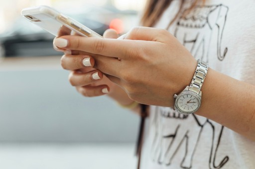 A close-up of a person's hands holding a smartphone, wearing a stylish watch, with a blurred background.