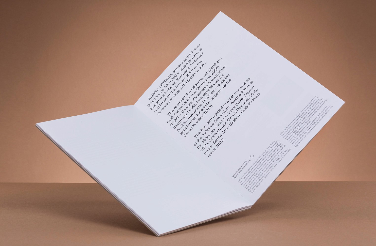 Open booklet featuring text about Eliana Heredia's background and artistic achievements against a neutral backdrop.