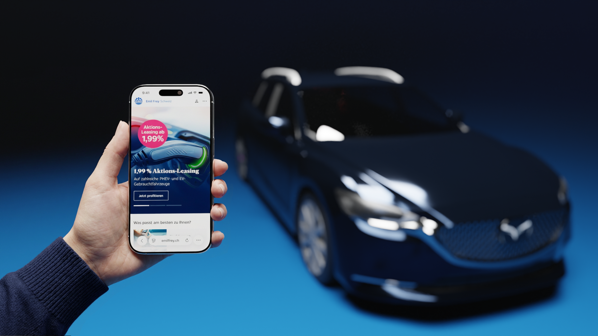 Eine Hand hält ein Smartphone, auf dessen Display die Homepage von Emil Frey Switzerland zu sehen ist. Dahinter ein verschwommenes Auto.