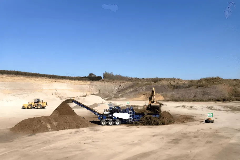 Green waste being mulched in a sand quarry with a digger and a loader