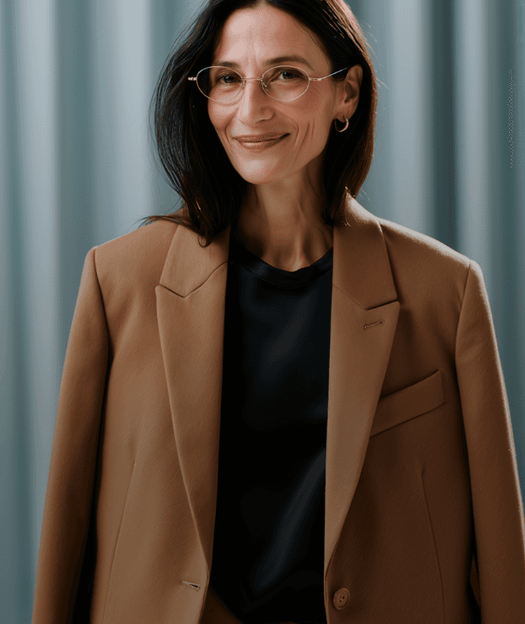 A professional woman in a brown suit and glasses, exuding confidence and poise.