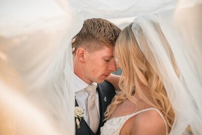 The newlyweds touch foreheads beneath a softly draped veil.