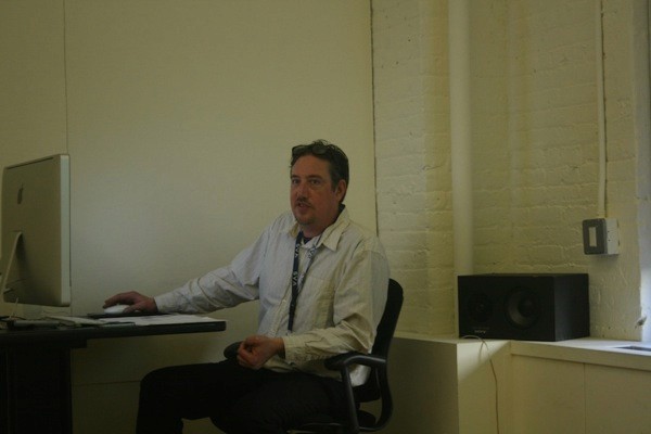 A photo of a teacher standing in a classroom and working on a computer.
