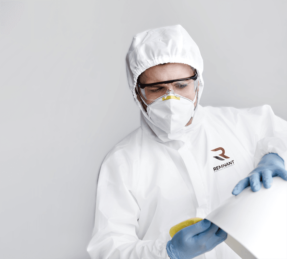 Woman in casual denim shirt interacting with a biohazard remediation worker in protective suit and gloves, with the 'REMNANT' logo visible on the suit.