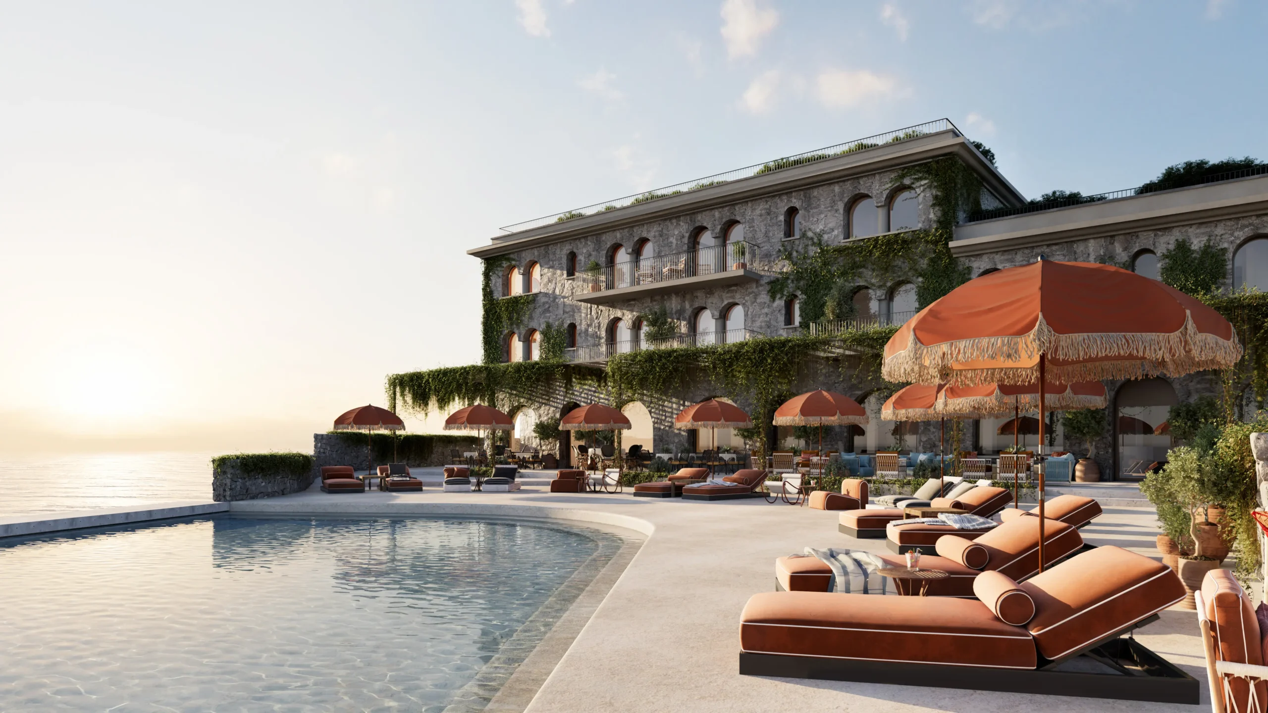Luxuriöser Außenpool eines Hotels aus Naturstein bei Sonnenuntergang. Gepolsterte Sonnenliegen mit orangefarbenen Sonnenschirmen säumen das Becken, die Fassade ist mit Efeu bewachsen.