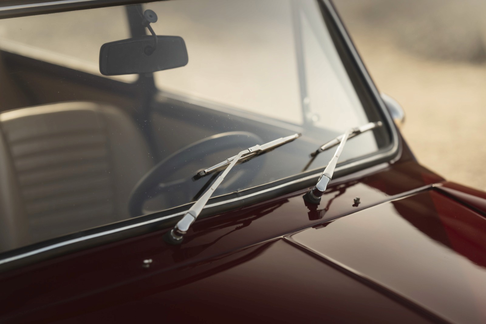 Close-up of a car's windshield wiper on a red vehicle, with sunlight reflected on the glass.