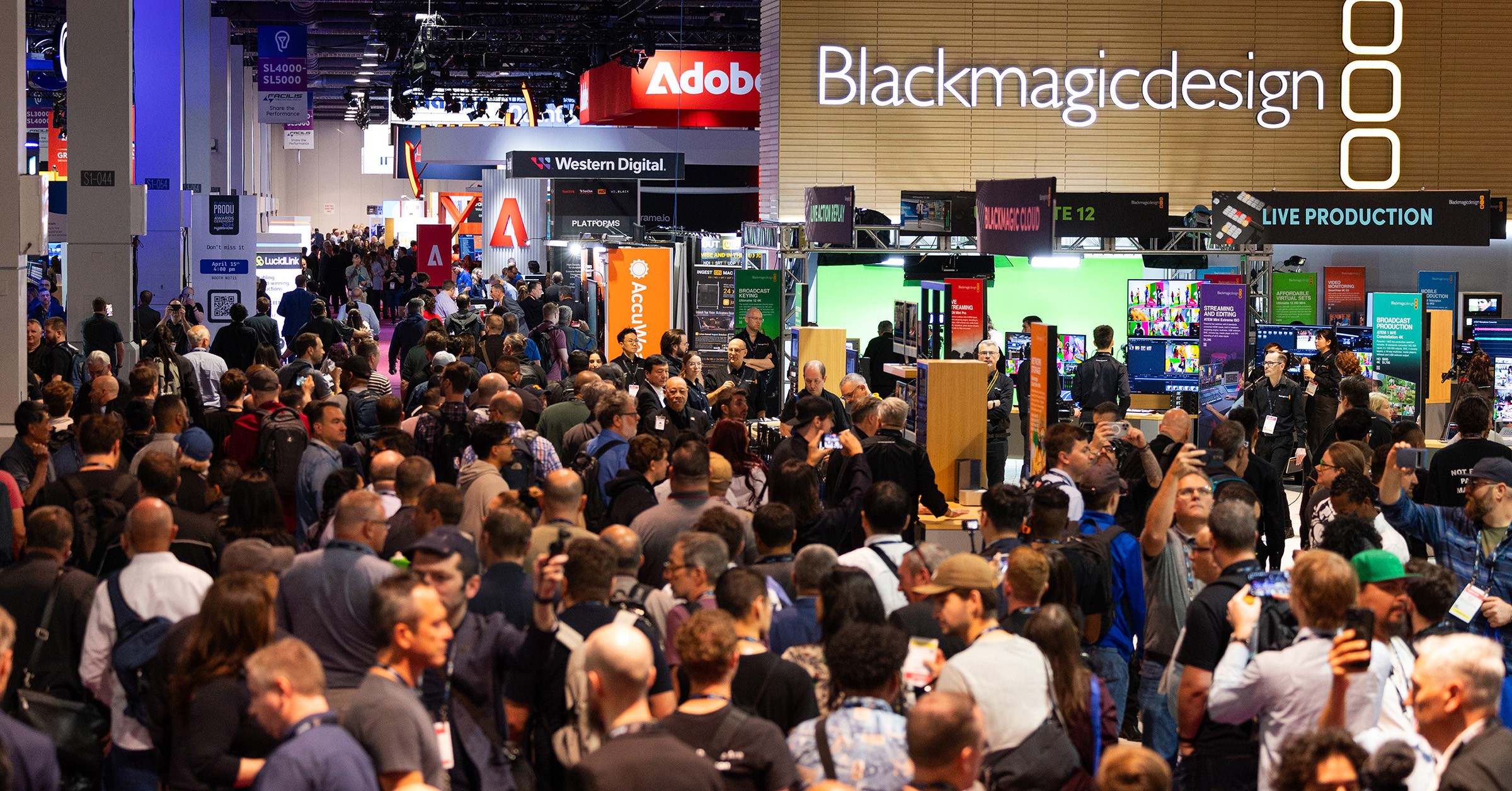 A crowded exhibition hall at the NAB Show in Las Vegas, featuring major broadcast technology brands like Blackmagic Design and Adobe, showcasing the scale of the global media and entertainment event.