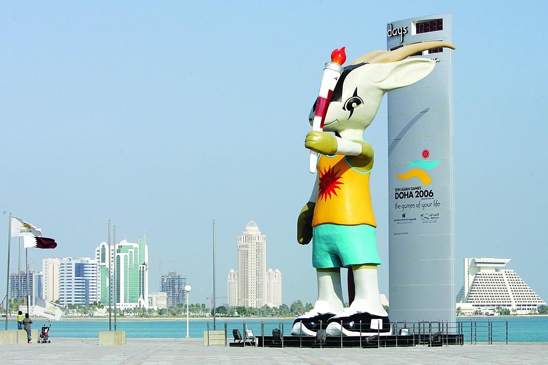 La mascotte des Jeux asiatiques de Doha 2006, sa torche à la main, devant la colonne du compte à rebours sur la Corniche, avec les tours de Doha derrière