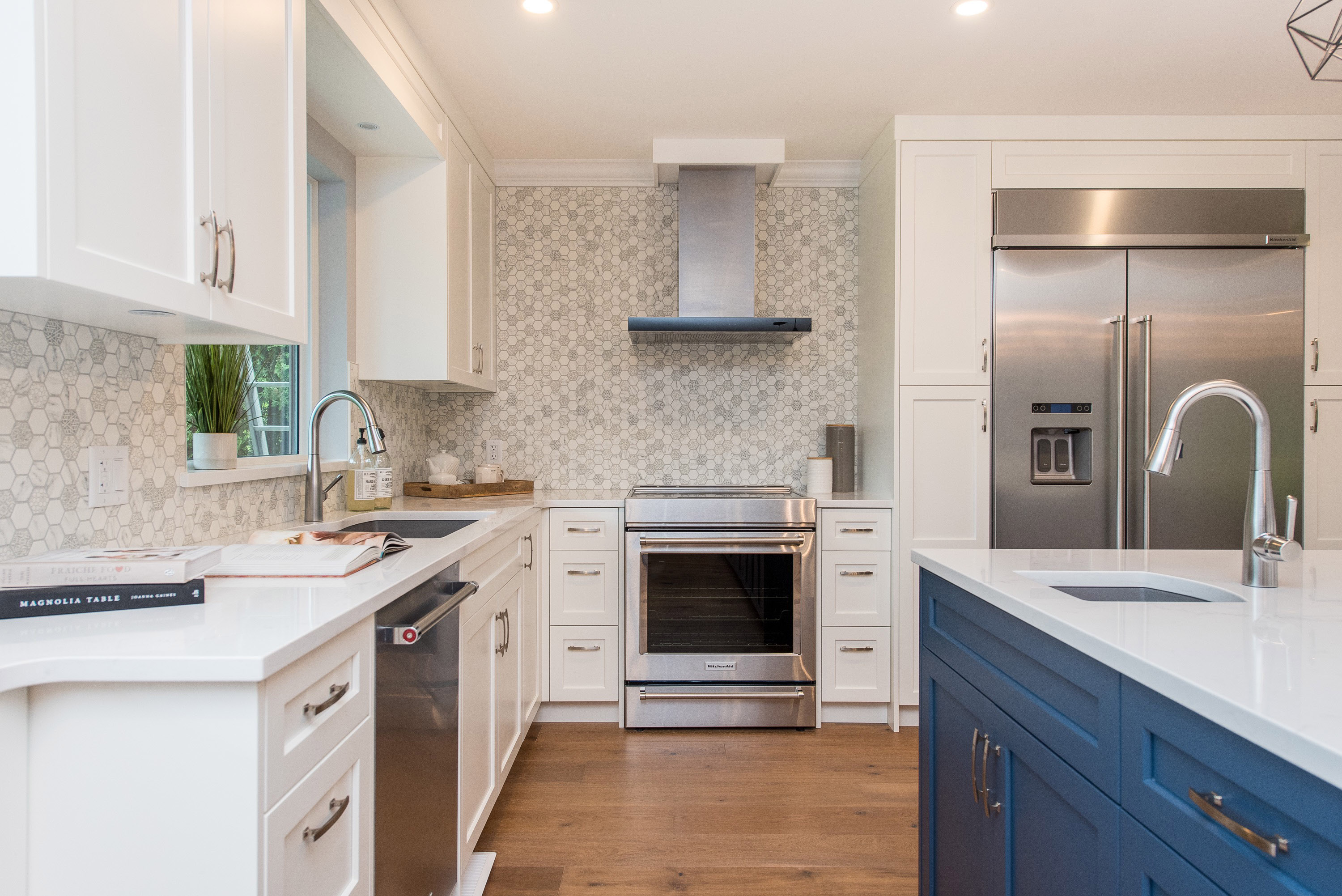Modern kitchen with white cabinets, stainless steel appliances, and a dark blue island, featuring hardwood floors.