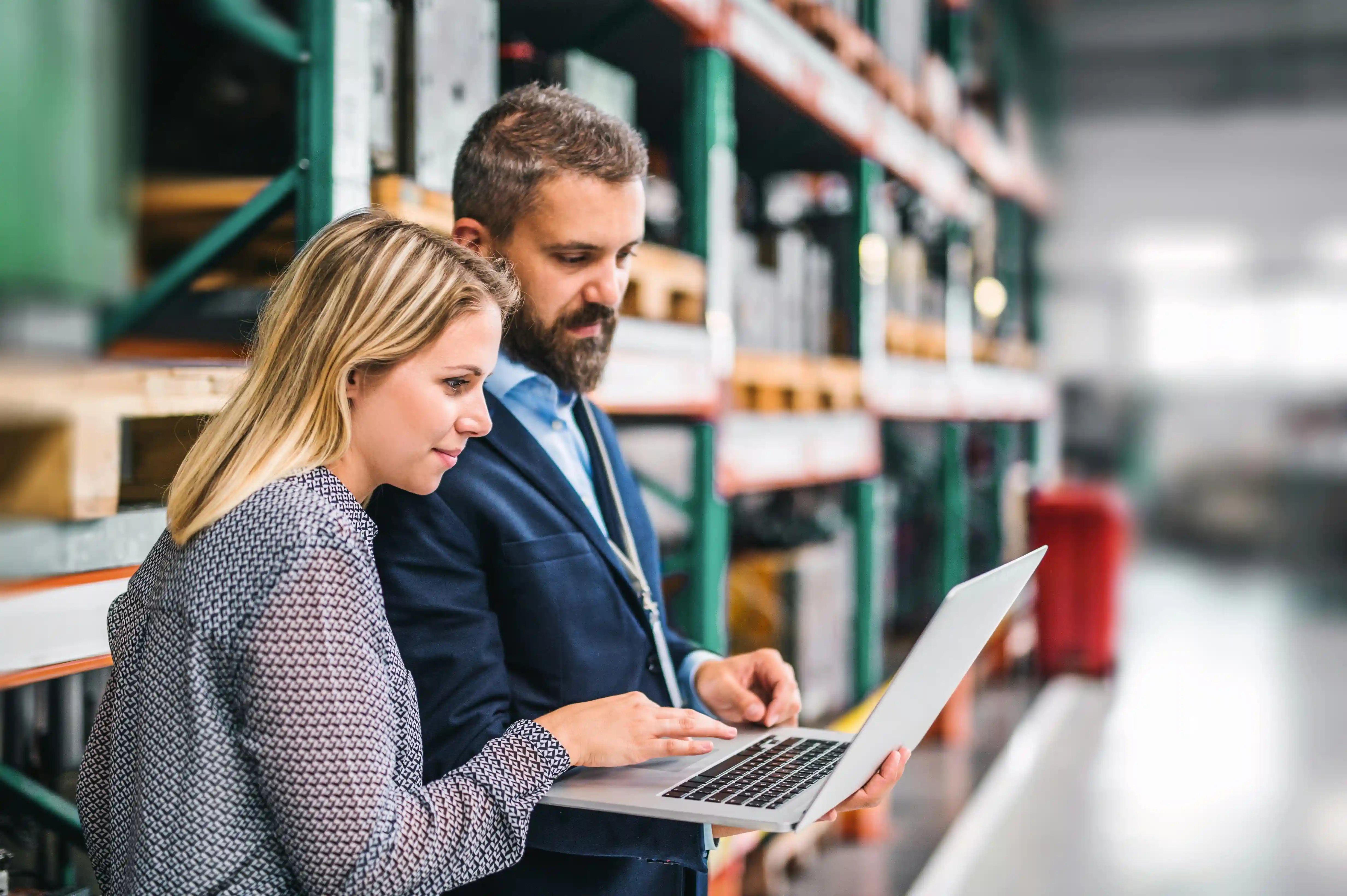 man and woman look at a laptop in a busy 3pl warehouse