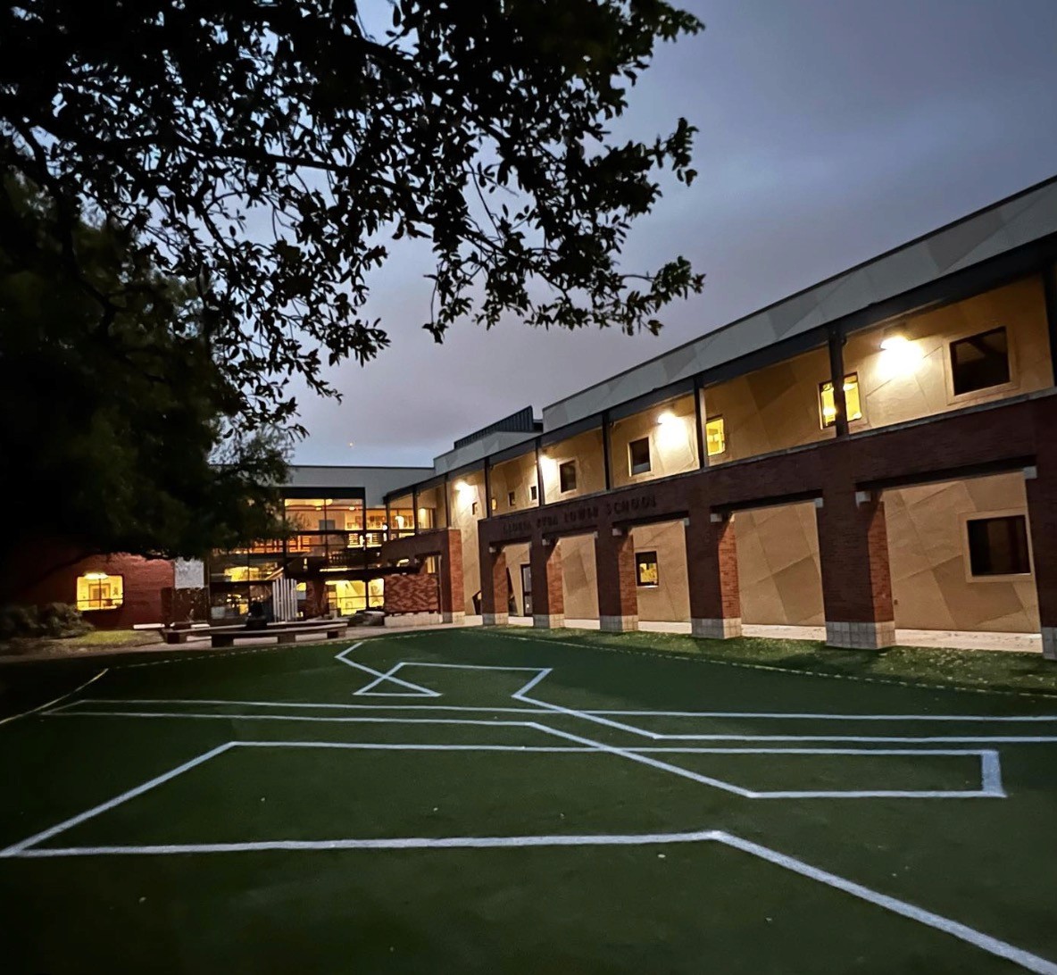 A low-lit view of a building with outdoor lights, surrounded by green grass and trees, creating a serene evening atmosphere.