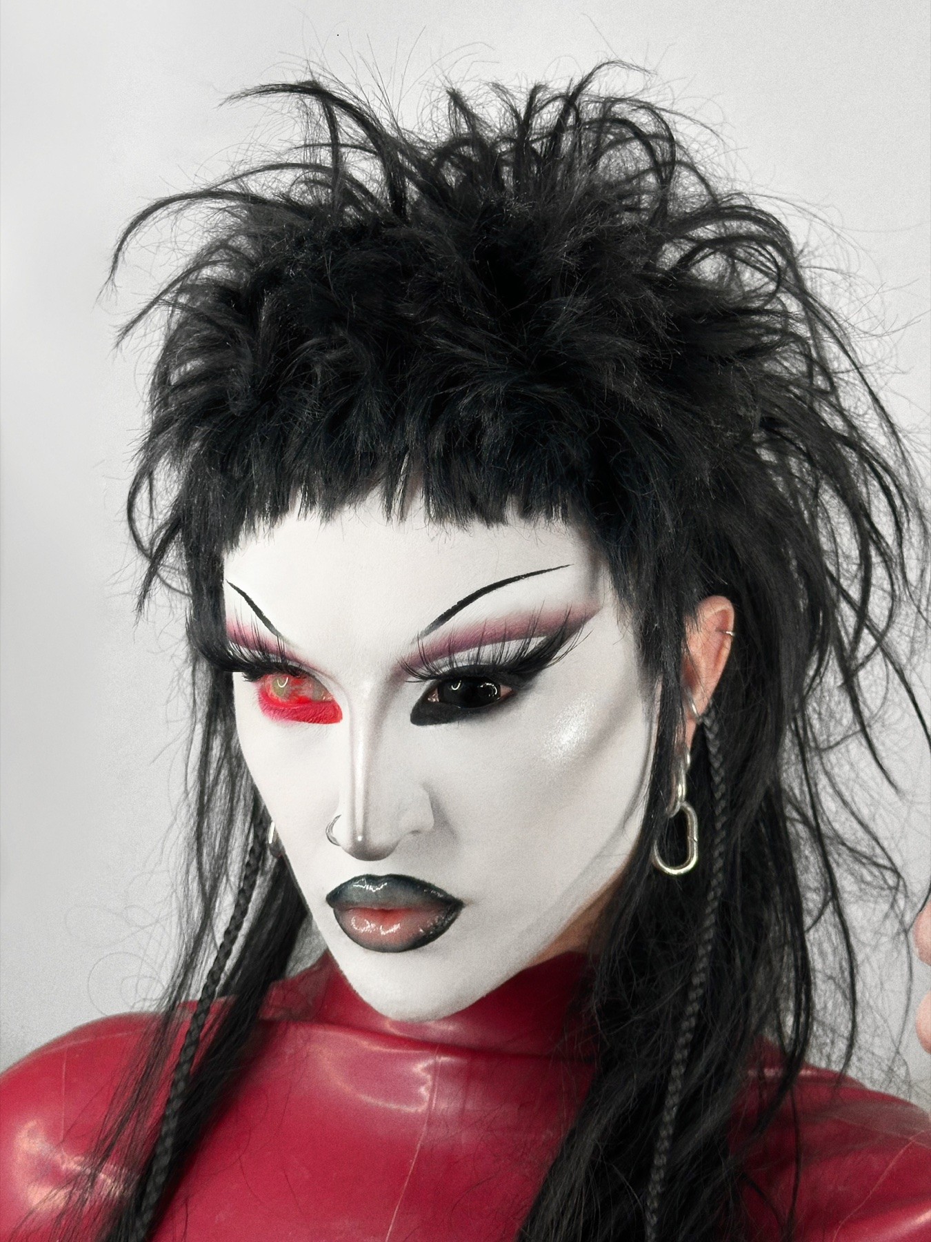 Bo Quinn in red latex with angular black hair and asymmetric red and black eye makeup