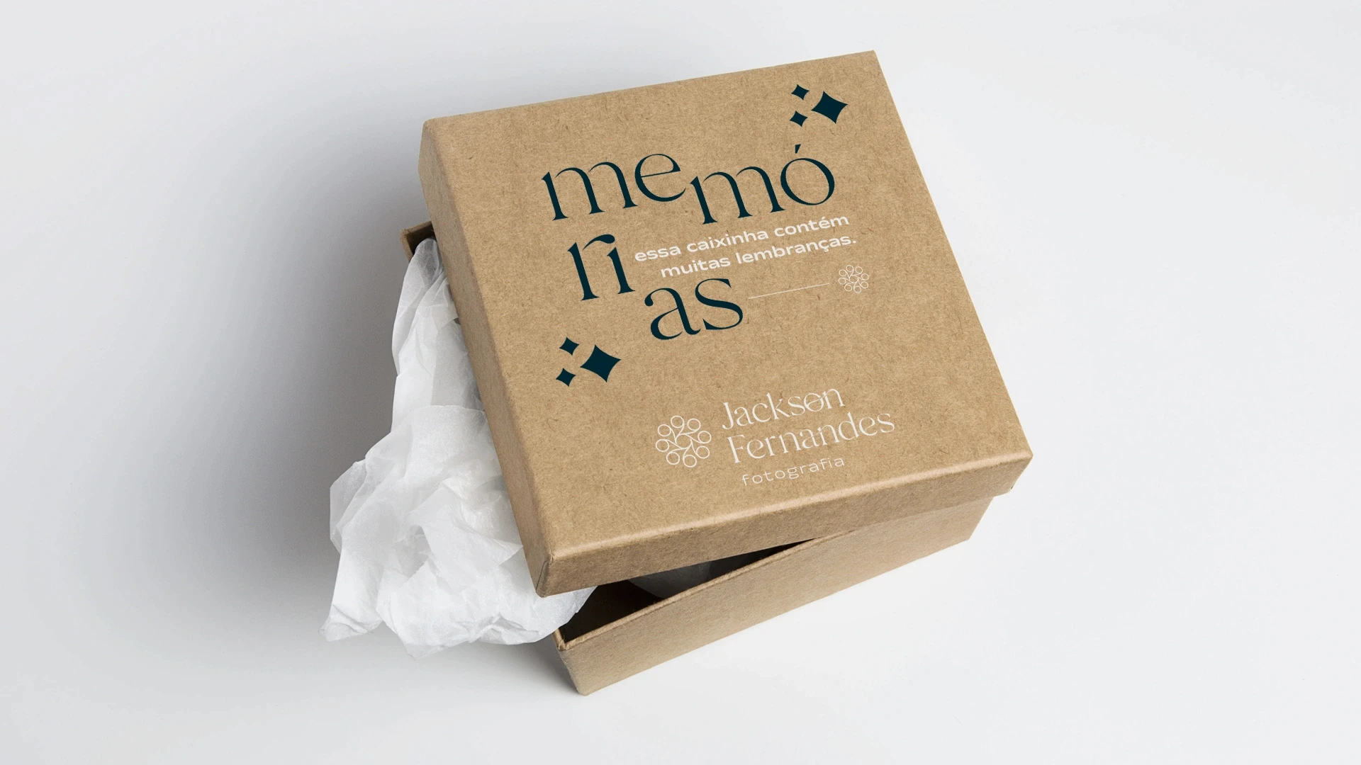 Caixa de papelão kraft levemente aberta contendo papel de seda branco em seu interior, com a tampa estampada em azul-escuro com a frase 'memórias - essa caixinha contém muitas lembranças' e o logotipo da marca.