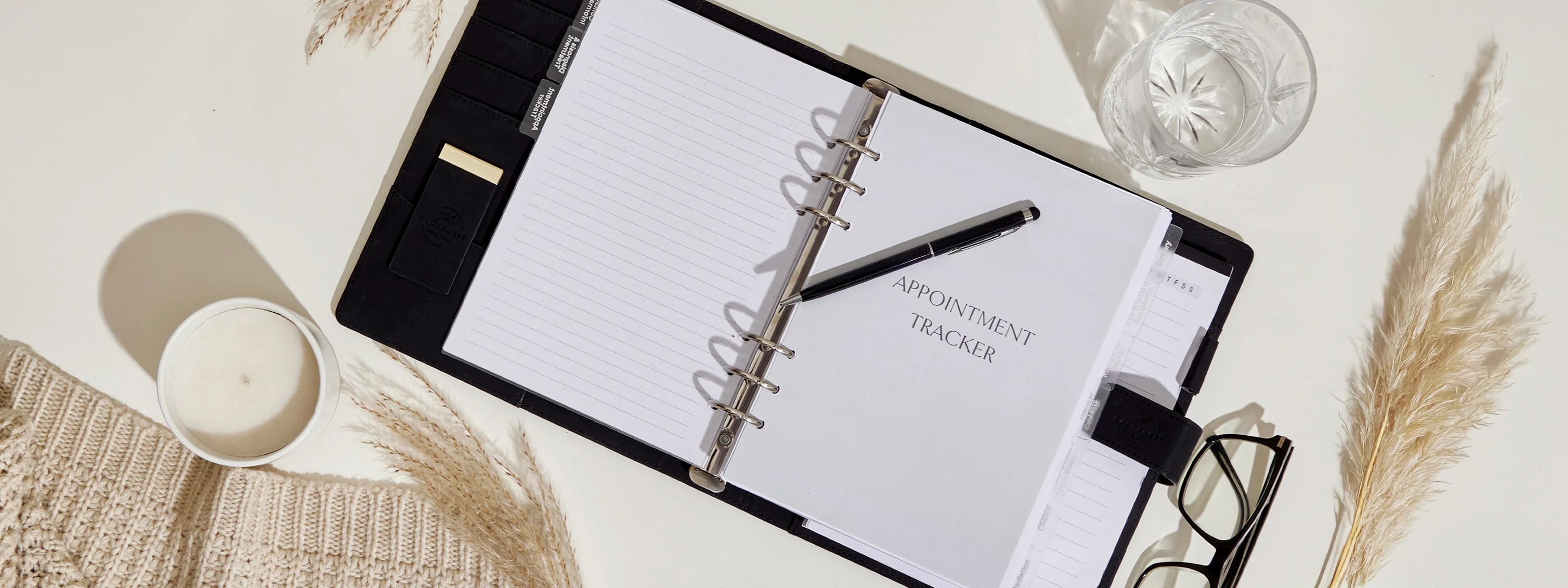 a neatly organized planner with the title "APPOINTMENT TRACKER," a pen, glasses, and a candle.