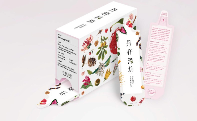 A white box with a floral design featuring various plants and flowers is shown. The box has text in both English and Chinese. A pink test strip is partially unrolled and lies beside the box. The packaging is primarily white with pink accents.