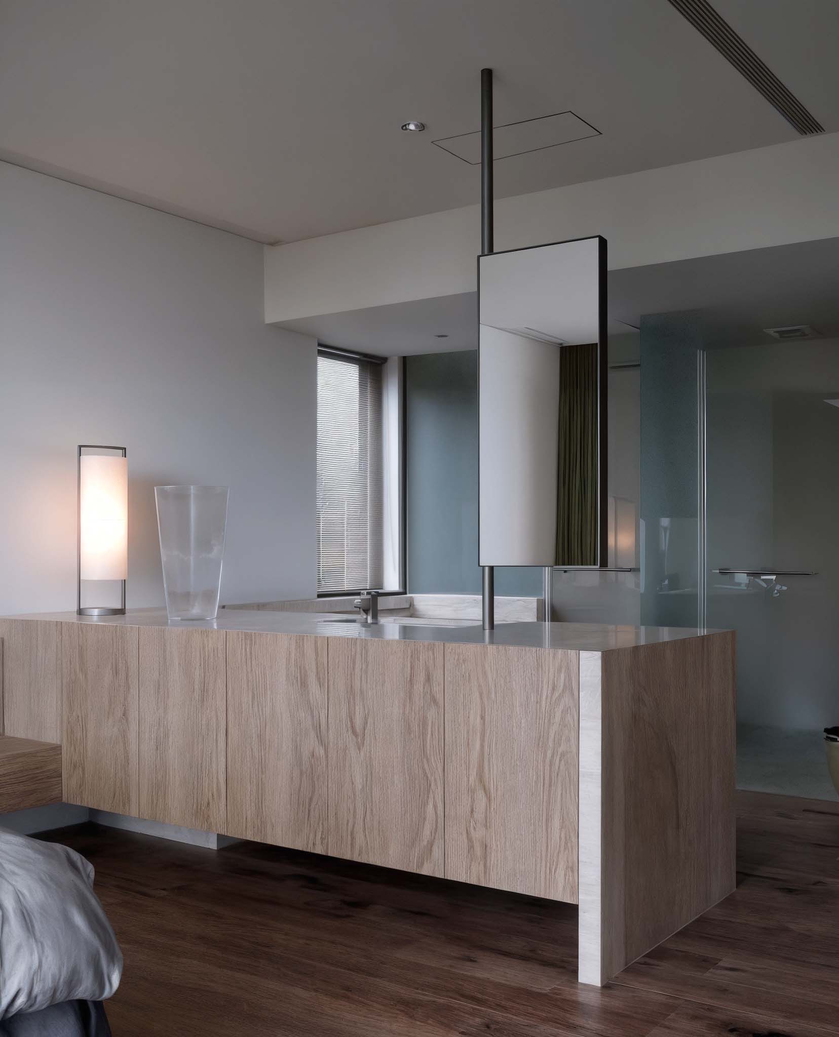 現代臥室空間延伸出木紋洗手台與立鏡設計，左側有立燈與玻璃杯裝飾，呈現低調奢華感