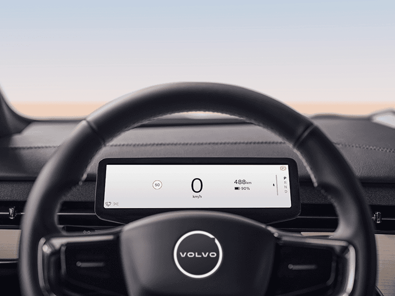 Image of a close-up VOLVO EM-90 steering wheel featuring a Volvo logo concept debossed onto the wheel. The steering wheel includes a digital display showing a GPS driving app.